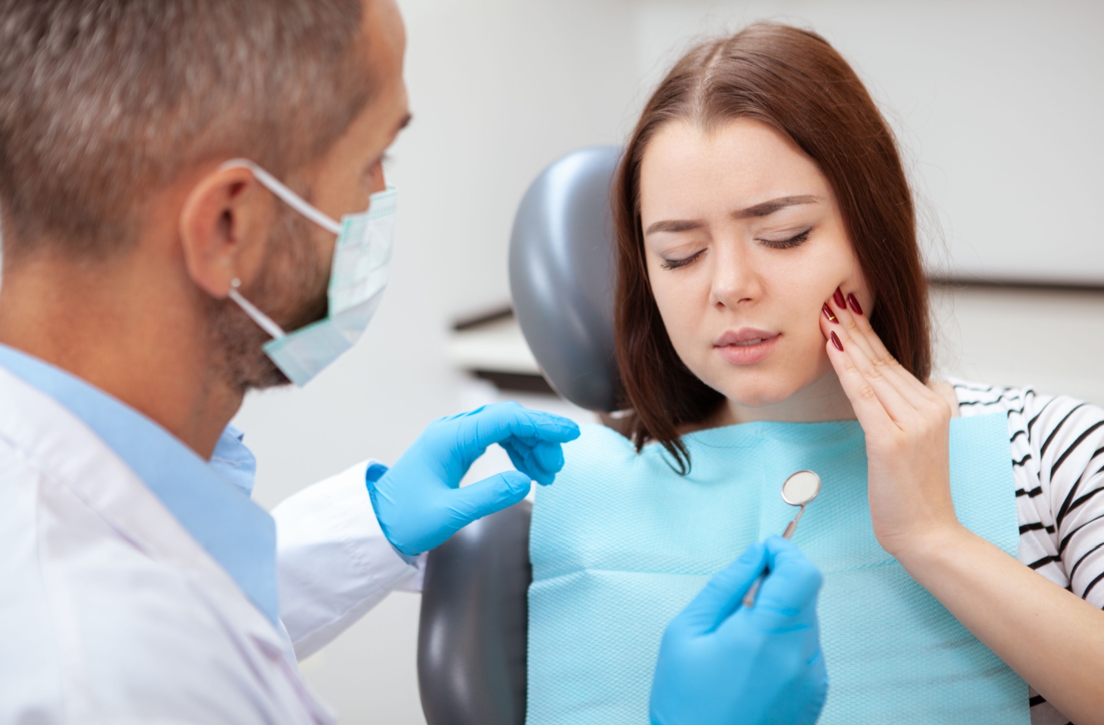 A young adult explains where their toothache is before the dentist examines their mouth and jaw.