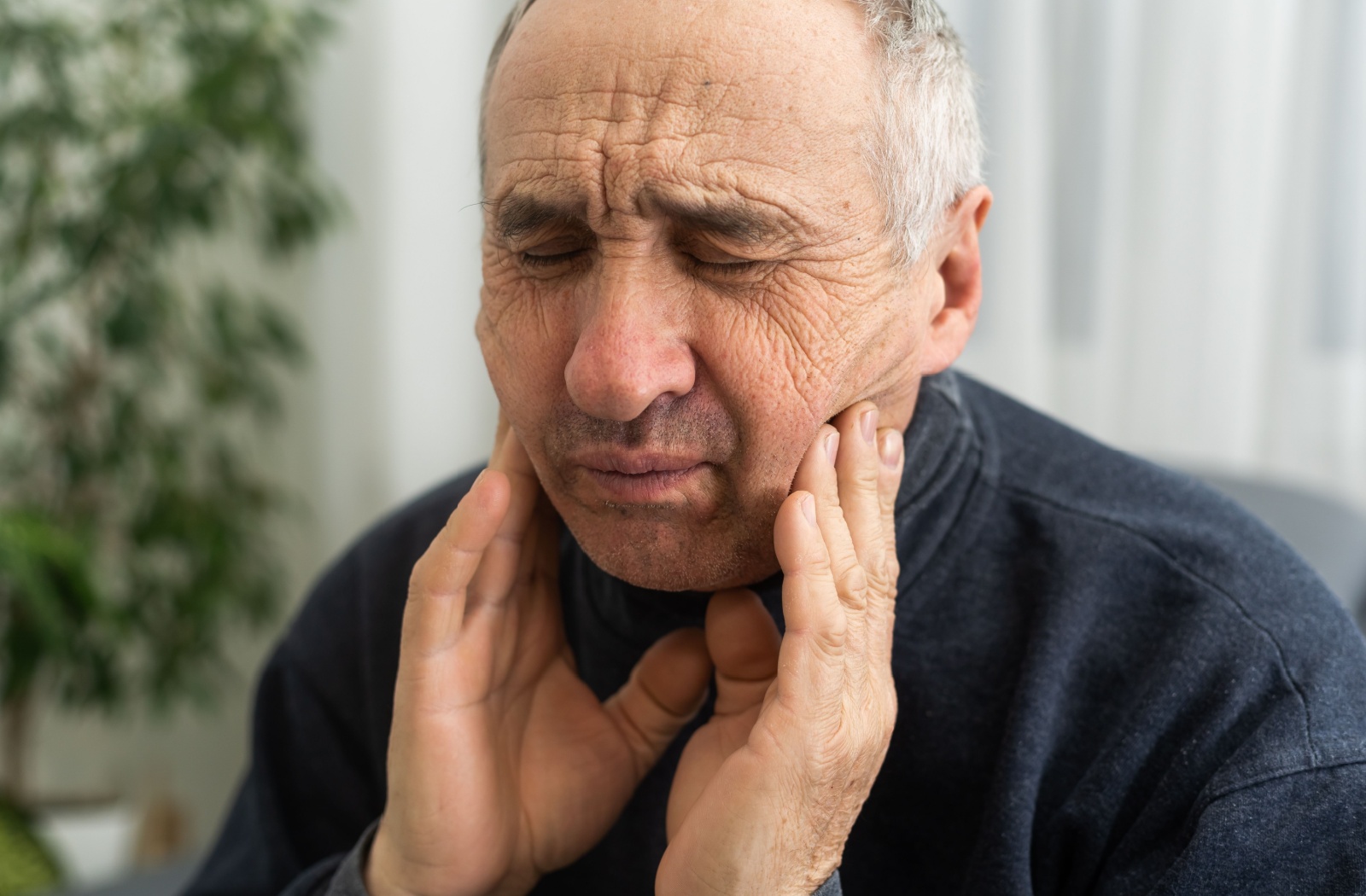 An older adult massages their jaw to try and alleviate the toothache pain causing a headache.