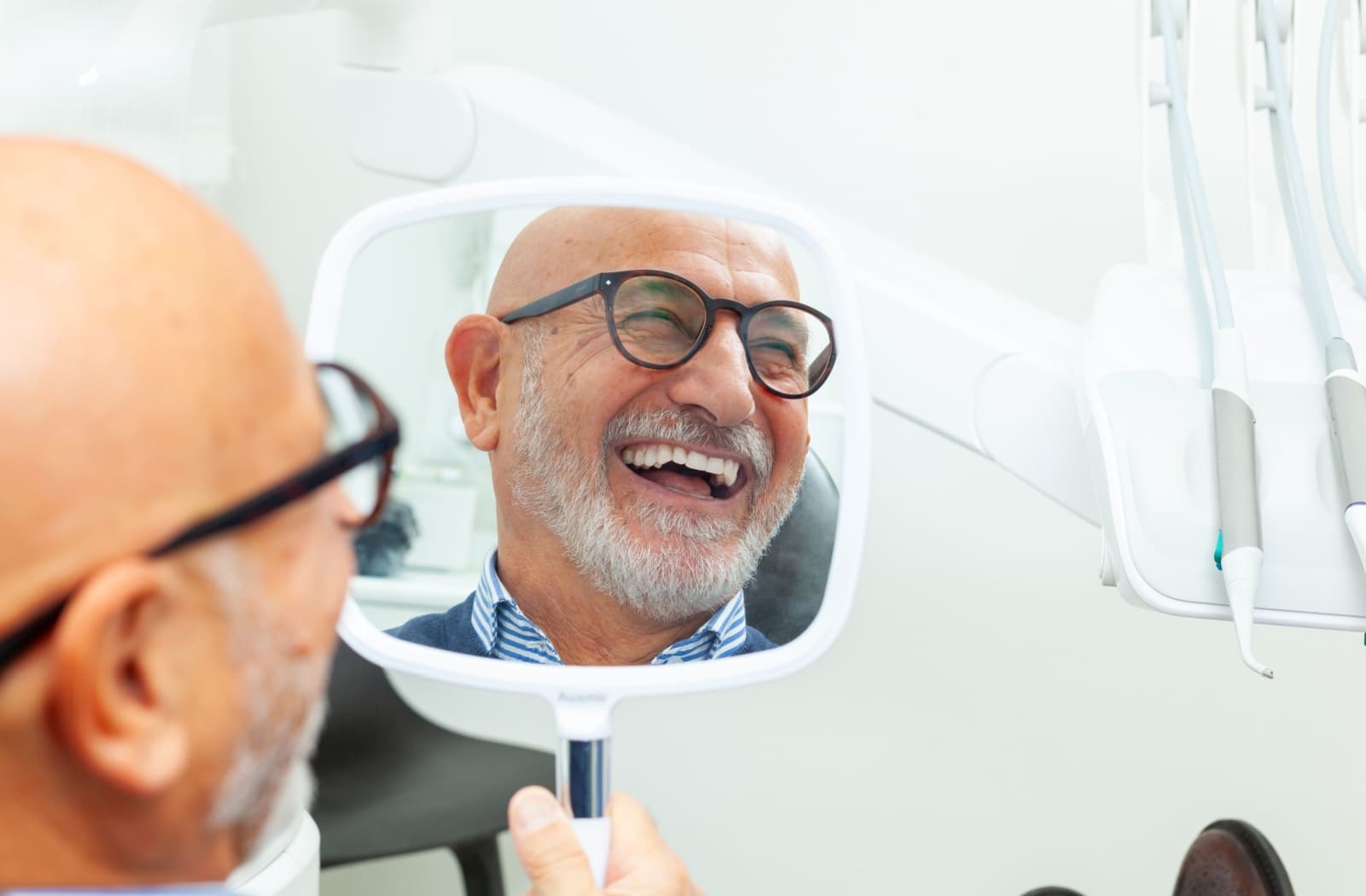 A person smiles into a handheld mirror after recovering from their tooth extraction.