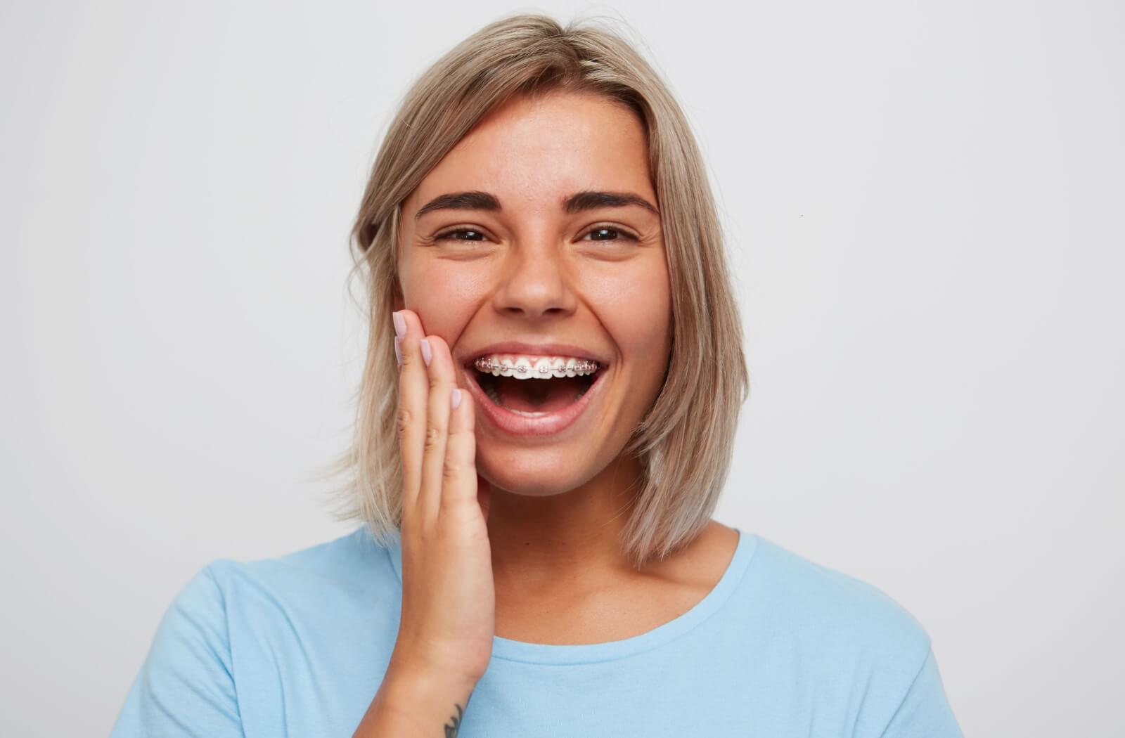 A person with a wide smile touches their cheek and shows off their braces.