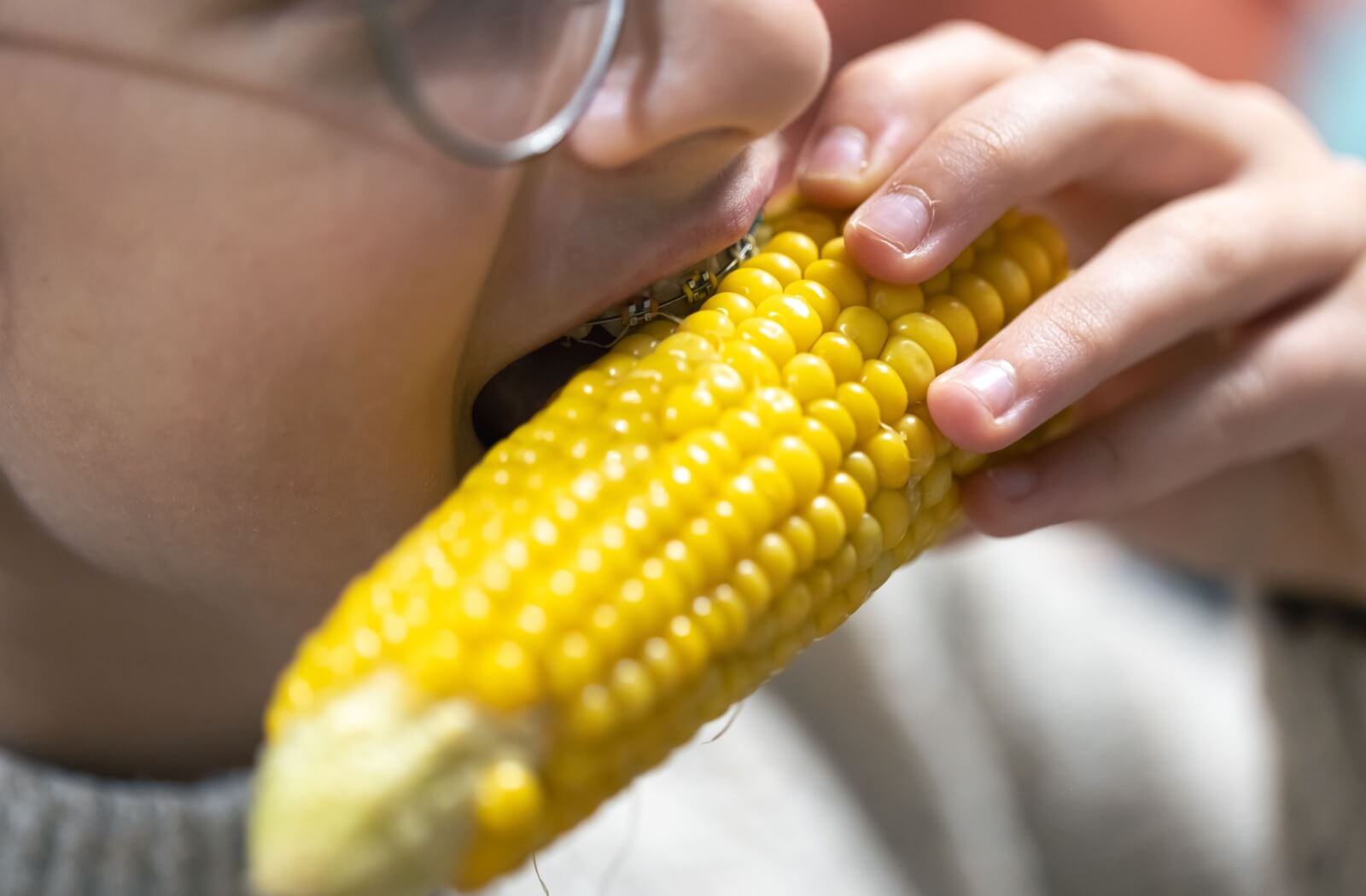 A person bites into a cob of corn while wearing braces, risking bending or breaking them with every bite.