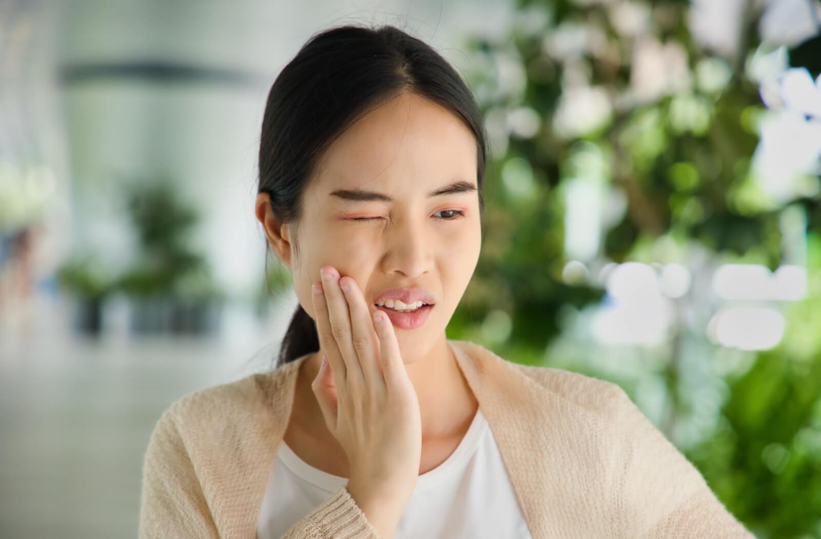 A young person holds their hand to their cheek as if they are in pain from their wisdom teeth growing in.