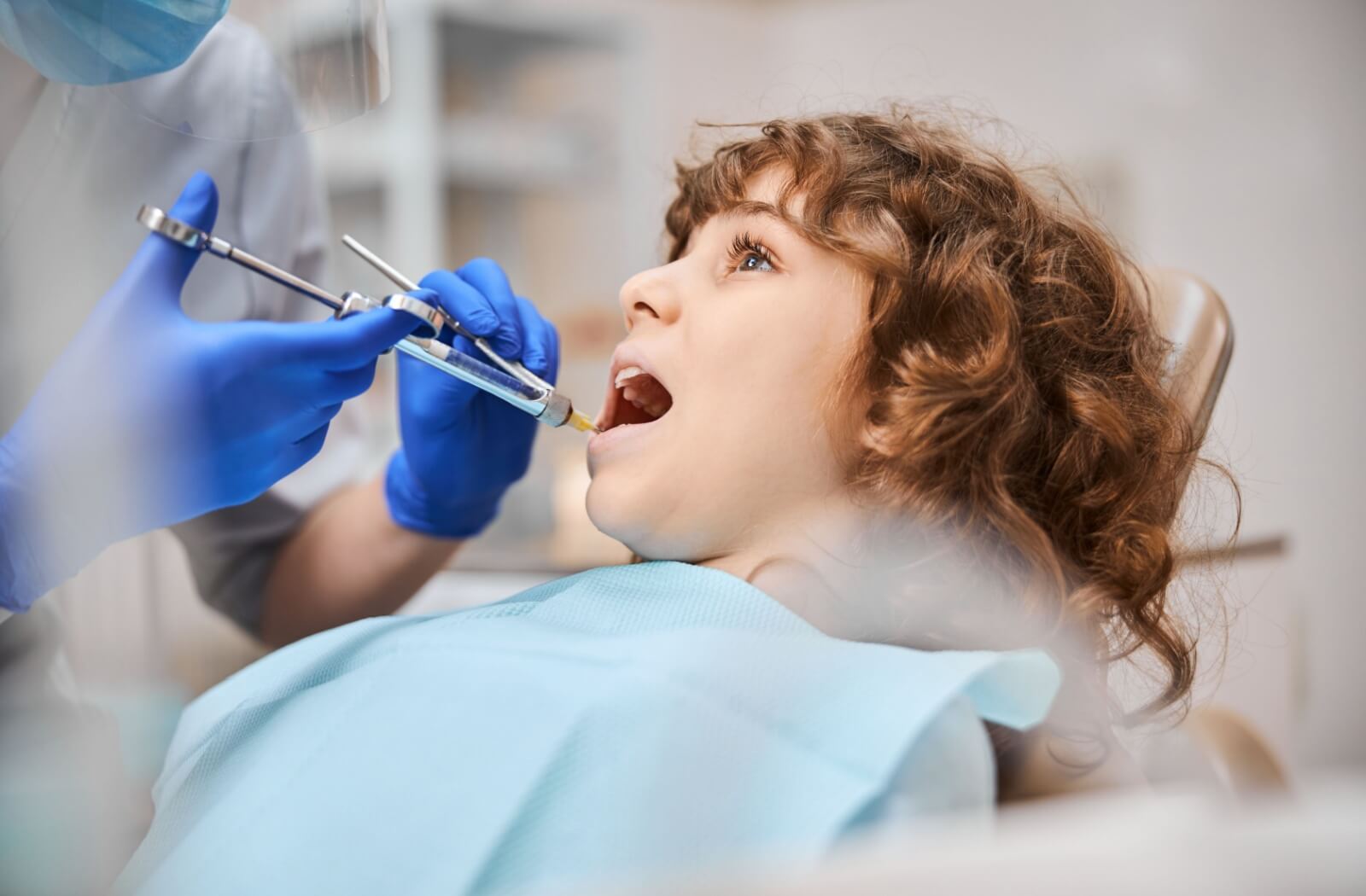 A child sits calmly while their dentist administers a local dental anesthetic.